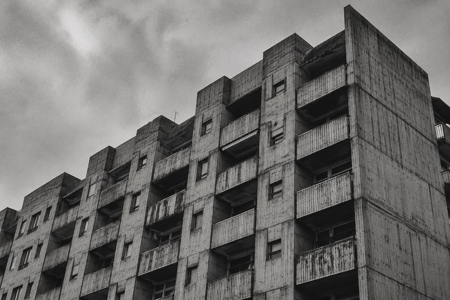 Weathered brutalist residential facade with balconies, overcast sky